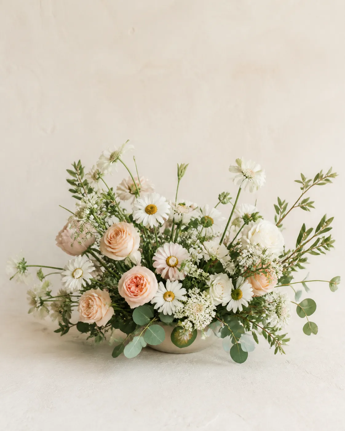A low table arrangement with daisies, soft roses and generous foliage